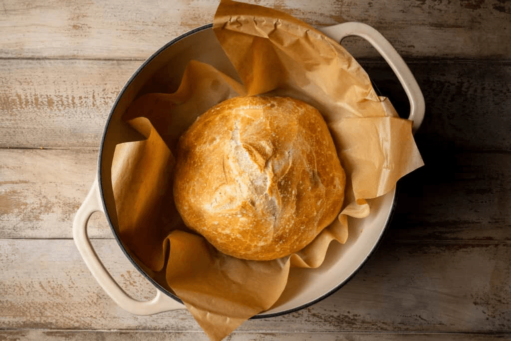 A golden no-knead loaf baked in a cream enameled Dutch oven